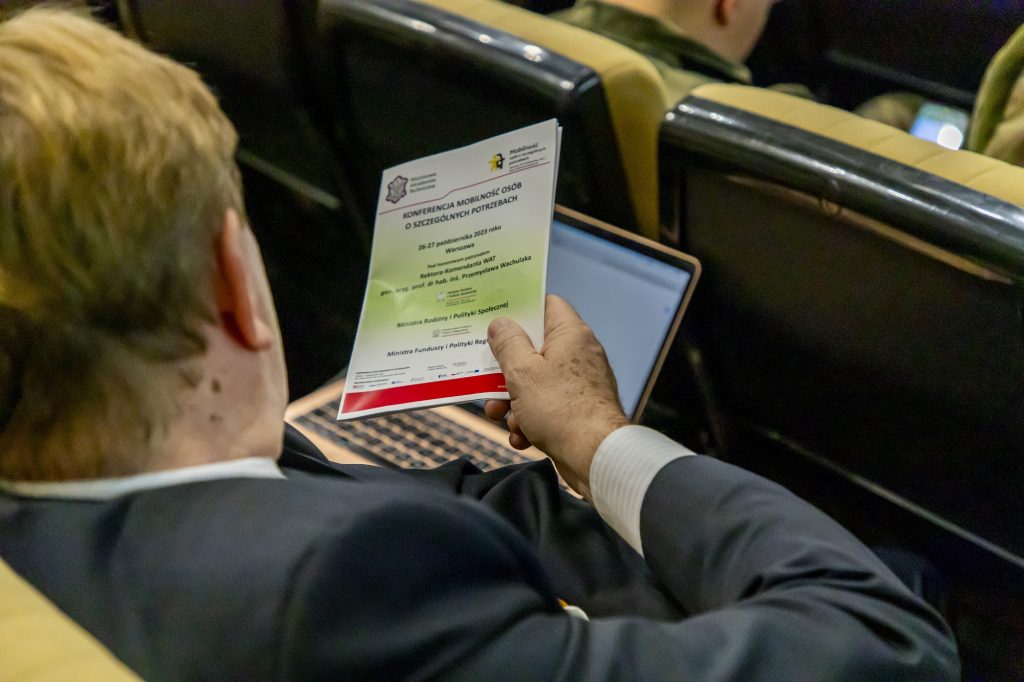 Jeden z uczestników konferencji siedzący tyłem do obiektywu, trzymający w ręku program konferencji