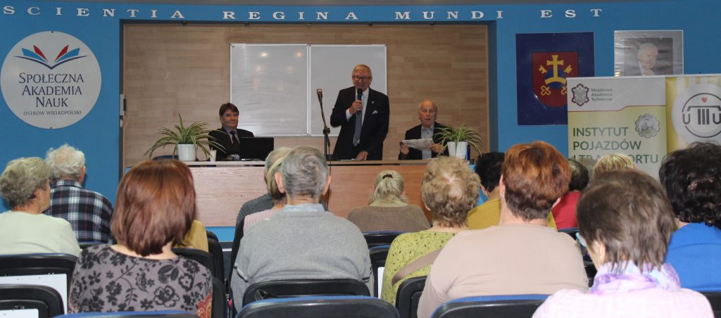 Uczesnicy seminarium, słuchacze Uniwersystetu Trzeciego Wieku w Ostrowie Wielkopolskim siedzący na sali szkoleniowej; na dalszym planie za stołem prezydialnym przedstawiciele Centrum Wiedzy o Dostępności oraz Uniwersytetu Trzeciego Wieku – stoi doktor habilitowany Jerzy Jackowski, profesor Wojskowej Akademii Technicznej, Dziekan Wydziału Inżynierii Mechanicznej, kierownik Centrum Wiedzy o Dostępności